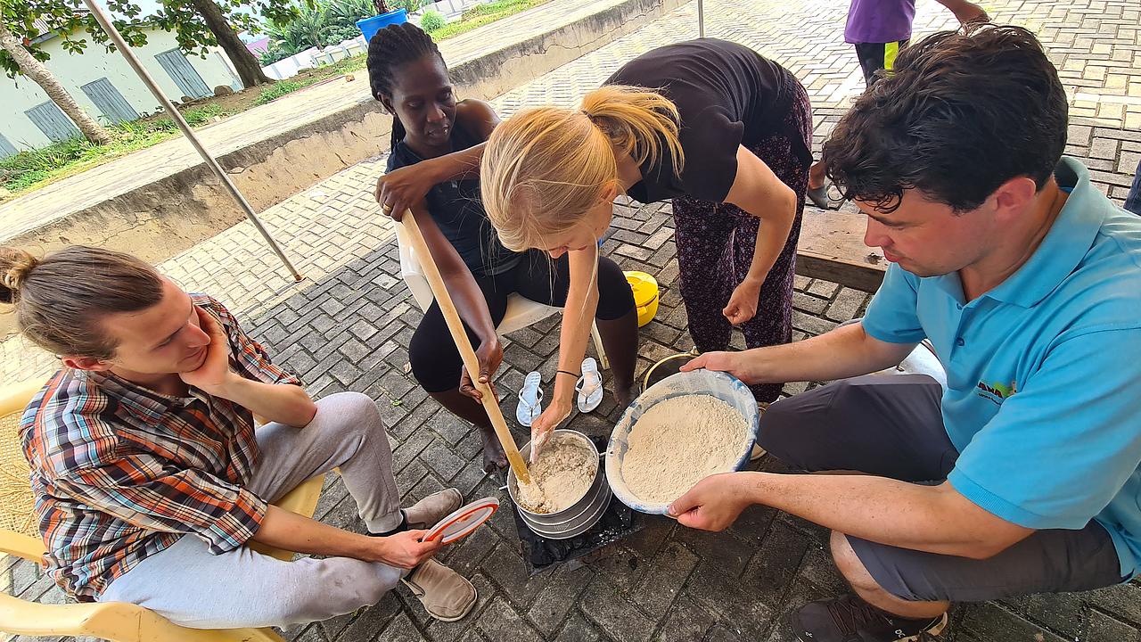 Mitglieder des Arbeitskreises kochen zusammen mit Einheimischen ein ghanaisches Gericht in Alutöpfen im Freien.