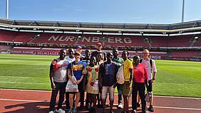 Gruppenfoto mit deutschen und ghanaischen Teilnehmenden im Inneren des Stadions, Rasen und Tribüne im Hintergrund.